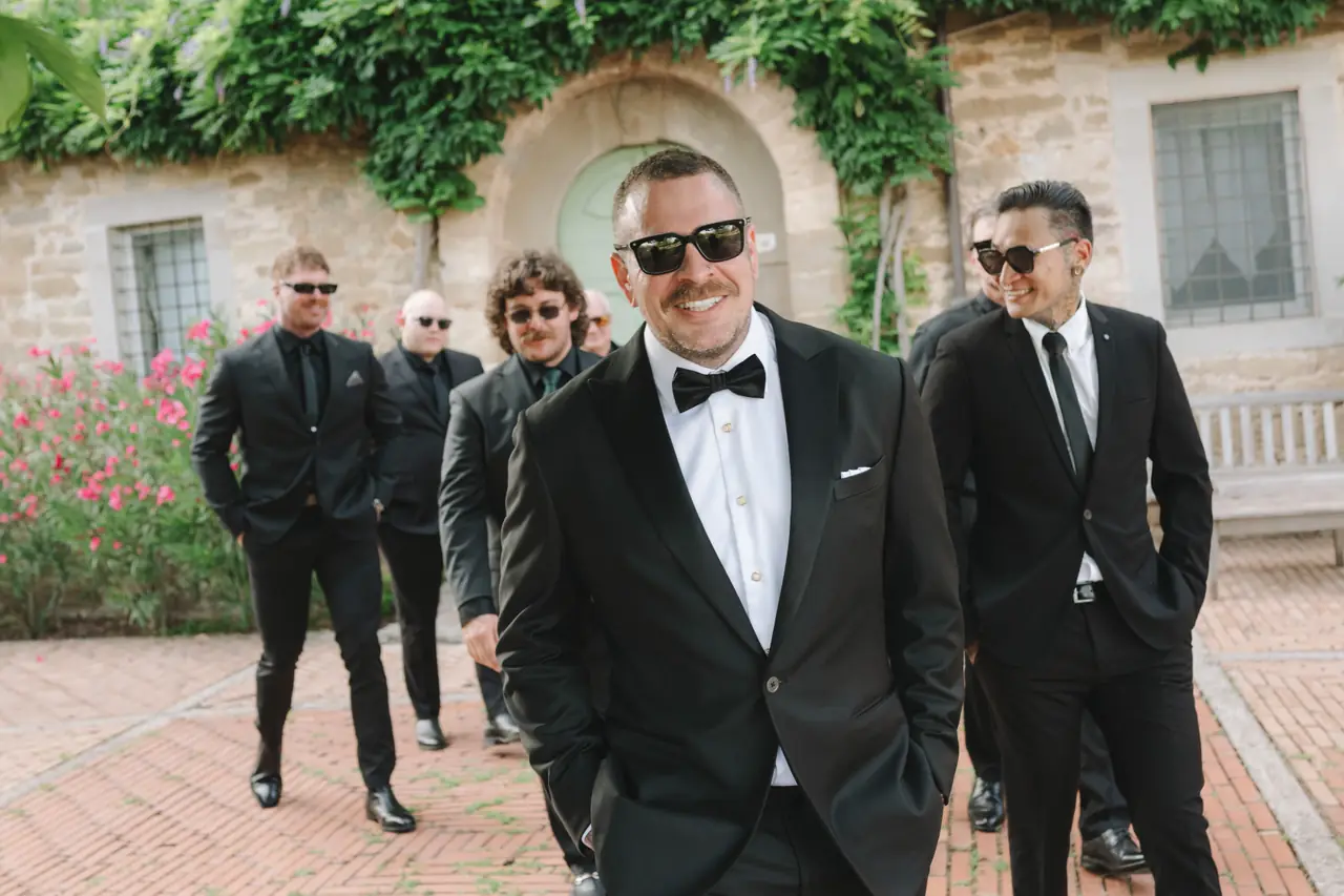 Anthony in a black tuxedo with his wedding party outside the stone villa.