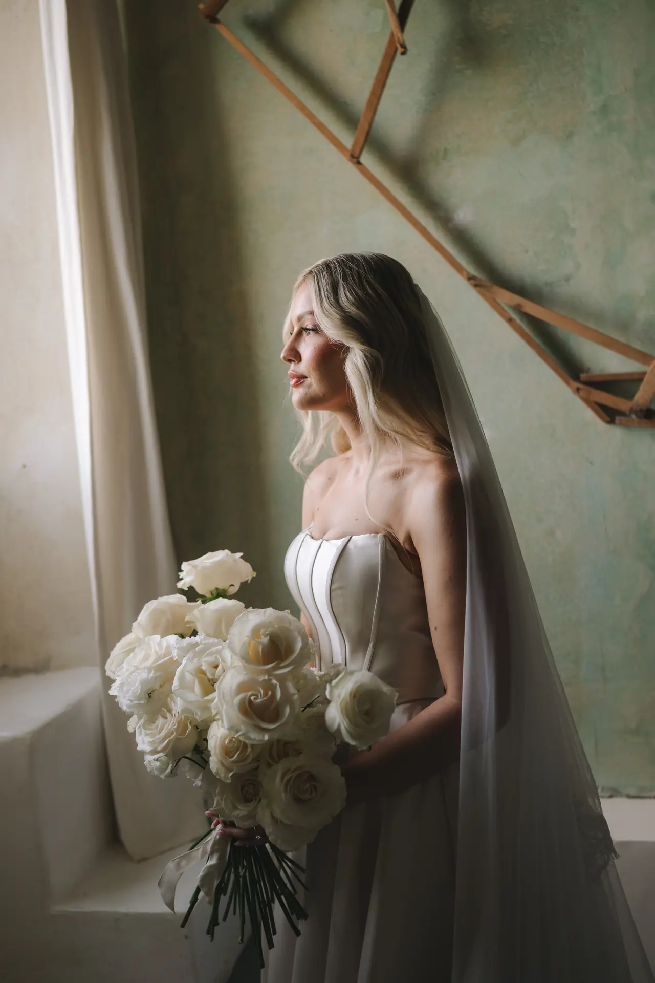 Isabella holds a white rose bouquet beside a window at Terzo di Danciano.