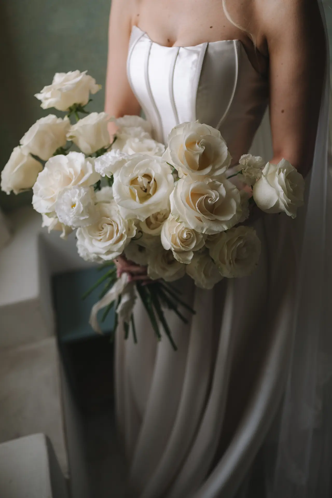 A close view of Isabella’s white rose bouquet and satin wedding gown.