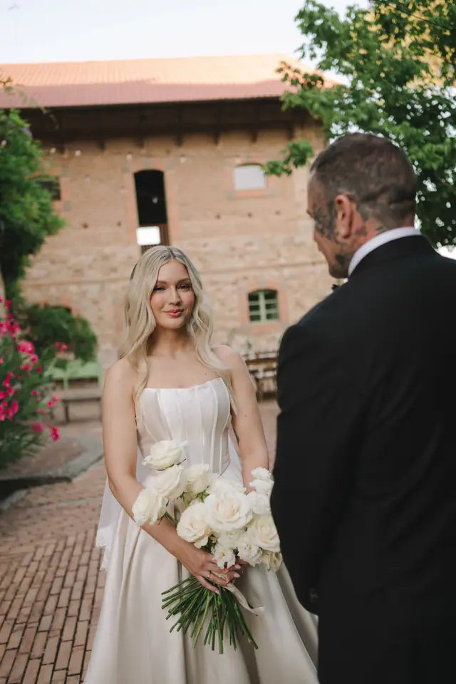 Isabella faces Anthony with her white rose bouquet in the courtyard.